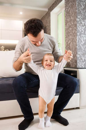 Father teaching a baby to walk in living room at homeの写真素材