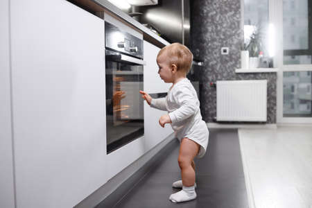 Infant baby boy near oven in home kitchen.の写真素材