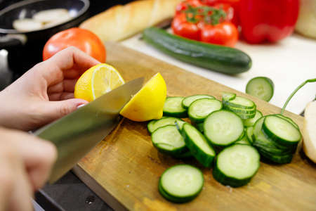 Young woman cut lemon for preparing salad in kitchen, close upの写真素材