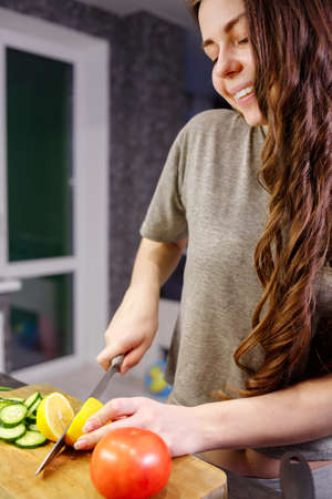 Young woman cut lemon for preparing salad in kitchen, close upの写真素材