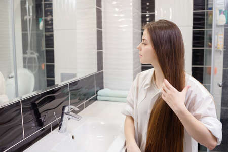 Young woman combing her long hair in bathroom after getting up in the morning.の写真素材