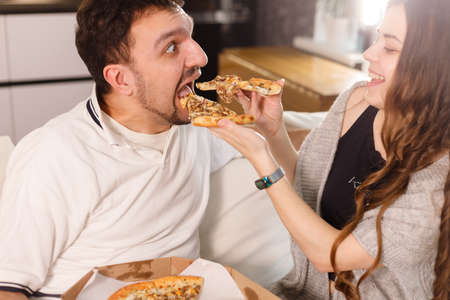 Girl feeds her husband with two slices of pizza. Exaggerate and wondering. Much credit on yourself and capabilities conceptの写真素材