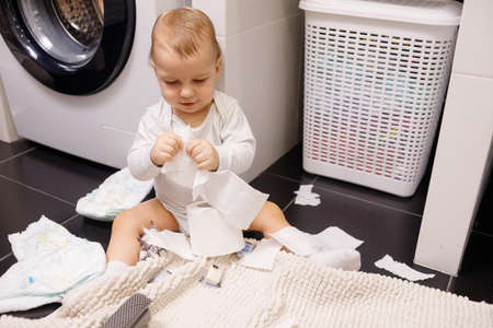 Infant or toddler baby tearing toilet paper and eat it. There are a lot of rolls on the floor. close-upの写真素材