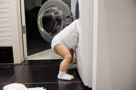 Child climbing into front-loading washing machine. side view. Lack of parental supervision.の写真素材