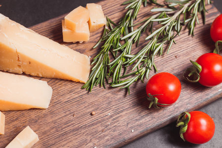 pieces of hard, aged cheese parmesan, fresh tomatoes and herbs on wooden boardの写真素材