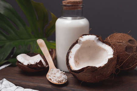 Glass bottle of milk or yogurt on dark wooden table with coconuts and coconut flakes in spoonの写真素材