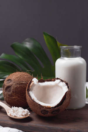 Glass bottle with milk or yogurt on dark wooden board with coconuts and flakes. tropical compositionの写真素材
