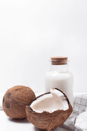 Coconut milk in a glass bottle. Whole and cracked coconut on white background