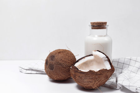 Coconut milk in a glass bottle. Whole and cracked coconut on white background
