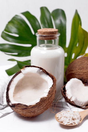 Coconut milk in a glass bottle. Whole and cracked coconut on white backgroundの写真素材