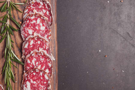 Smoked ham sausage and cutted slices with rosemary and cherry tomatoes on dark wooden board. Top view, flat layoutの写真素材