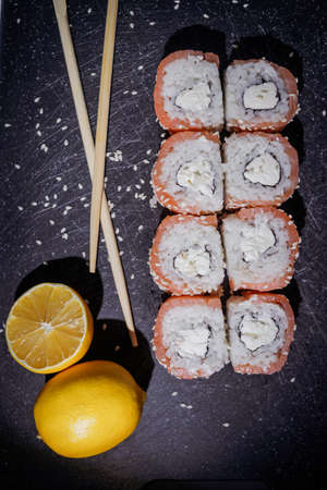 Sushi philadelphia rolls set served with lemon and souce on black board on dark background. Flat layout on black, top viewの写真素材