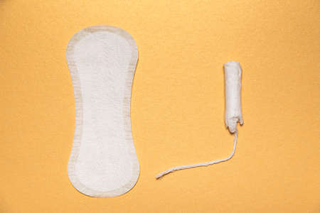 Sanitary napkin and tampon on golden background flat lay. Concept of choosing the most suitable for female hygieneの写真素材