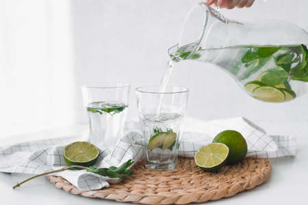 Detox water with lime fruit. Hand pouring lime fruit water from jug into glasses.の写真素材