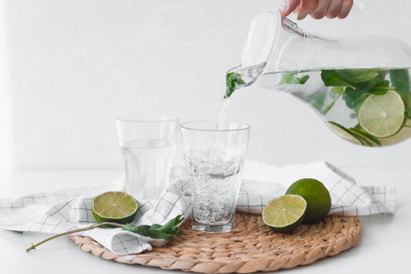 Detox water with lime fruit. Hand pouring lime fruit water from jug into glasses.の写真素材
