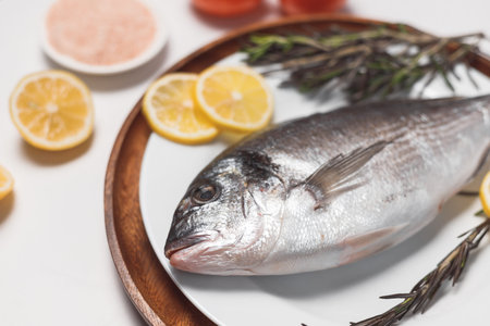 Raw dorada fish or gilt-head bream served on white plate on white background, flat lay, top view