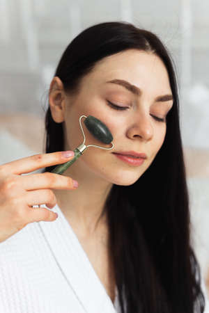 Beautiful european woman uses jade roller to massage her face. Spa self beauty treatmentの写真素材