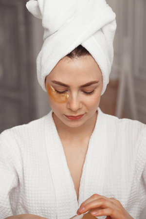 Pretty european girl applying golden collagen patches under her eyes. woman facial treatment. Cosmetology, beauty and spaの写真素材