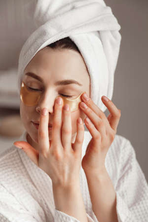 Pretty european girl applying golden collagen patches under her eyes. woman facial treatment. Cosmetology, beauty and spaの写真素材