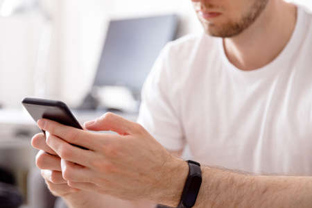 Man using modern smartphone device while sitting on sofa at home, modern design interiorの写真素材