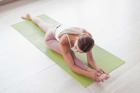 The sports girl the trainer is warming up is engaged in stretching sits on the twineの写真素材