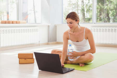 Young fit woman in sportswear watching online video with fitness exercises on laptop and doing push ups at home. Pretty lady burning calories, practice pilates. Distant training with personal trainerの写真素材