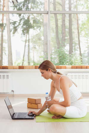 Young fit woman in sportswear watching online video with fitness exercises on laptop and doing push ups at home. Pretty lady burning calories, practice pilates. Distant training with personal trainerの写真素材