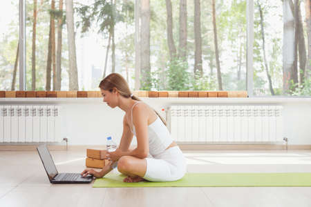 Young fit woman in sportswear watching online video with fitness exercises on laptop and doing push ups at home. Pretty lady burning calories, practice pilates. Distant training with personal trainerの写真素材