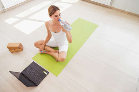Woman in sportswear drinking water and doing sport at home with laptop onlineの写真素材