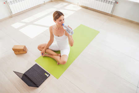 Woman in sportswear drinking water and doing sport at home with laptop onlineの写真素材