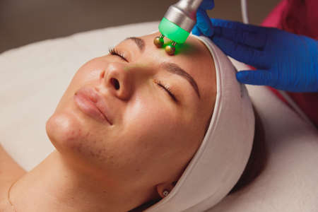 Young woman with acne getting ultrasound skin cleansing and face treatment at beauty salonの写真素材