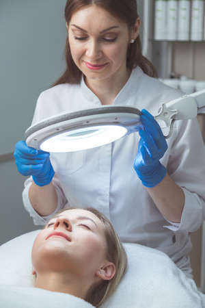 Beautician doctor is examining womans face with special lampの写真素材