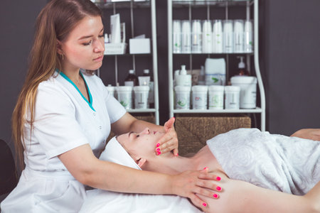 Girl masseur makes facial massage for a young lady in the beauticians office.の写真素材