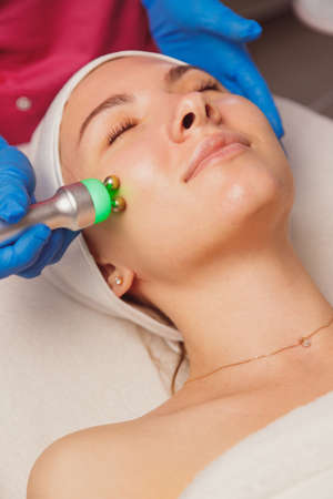 Young woman getting microcurrents skin cleansing and face treatment at beauty salon. Beautician takes care of her faceの写真素材