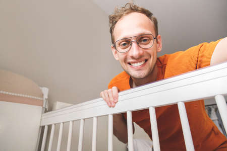 Young happy caucasian father looking at his baby in cribの写真素材