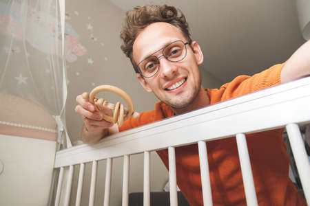 Young happy caucasian father looking at his baby in crib shaking with toy.の写真素材