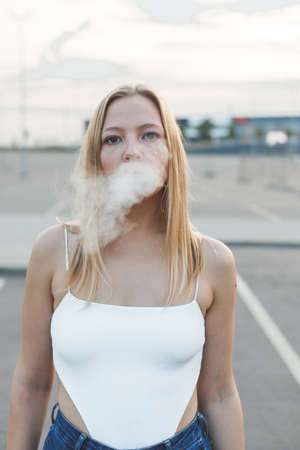 Blonde woman in city with electronic cigar vapingの写真素材
