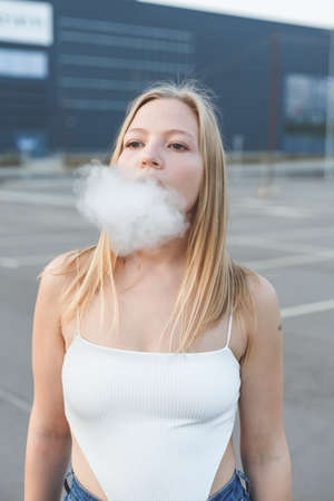 Blonde woman in city with electronic cigar vaping in white t-shirt outdoorsの写真素材
