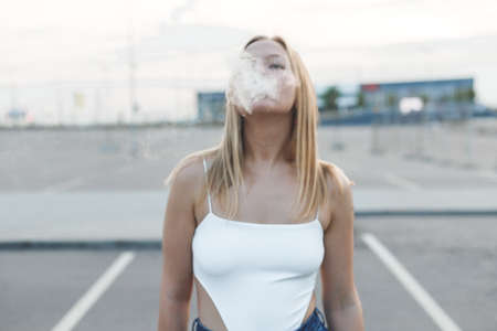 Blonde woman in city with electronic cigar vapingの写真素材