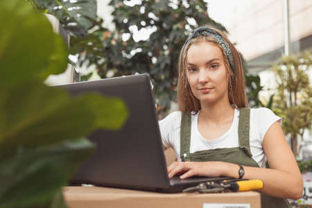 Blonde hipster woman freelancer working on laptop computer in houseplant storeの写真素材