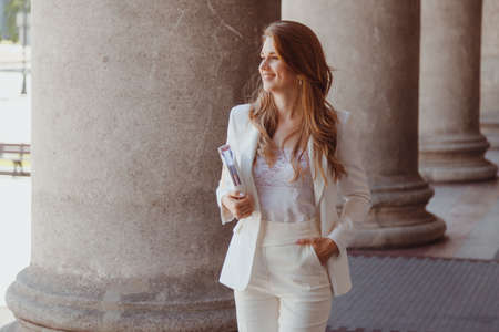 Happy young woman in white jacket with diary walks looking awayの写真素材