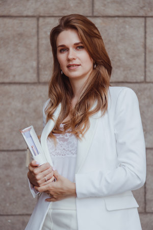 Confident elegant woman in white blazer with diary standing outdoorsの写真素材