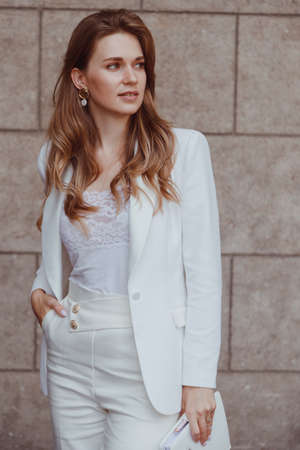 Confident elegant woman in white blazer outdoors looking away. Business style.の写真素材