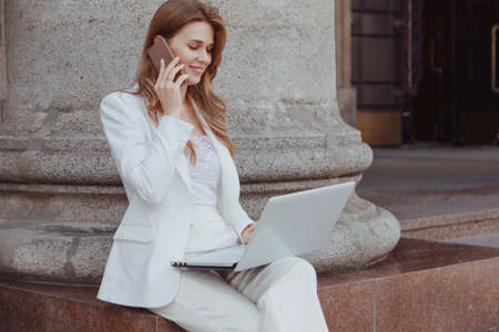 Young woman using smartphone and laptop outside a cafeの写真素材