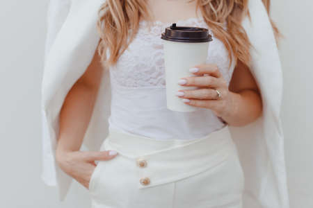 White paper disposable cup with hot drink in female hands weared in white suit.の写真素材