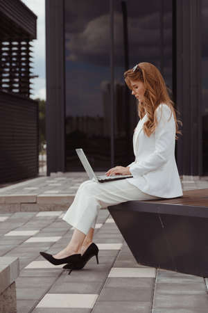 Young business woman in white suit working outdoor on laptopの写真素材