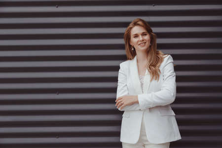 Portrait of caucasian business woman in white suit on metal gray backgroundの写真素材