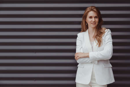 Portrait of caucasian business woman in white suit on metal gray backgroundの写真素材