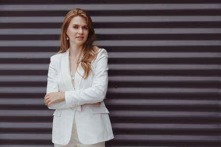 Portrait of caucasian business woman in white suit on metal gray backgroundの写真素材