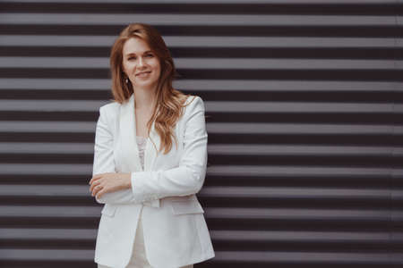 Portrait of caucasian business woman in white suit on metal gray backgroundの写真素材